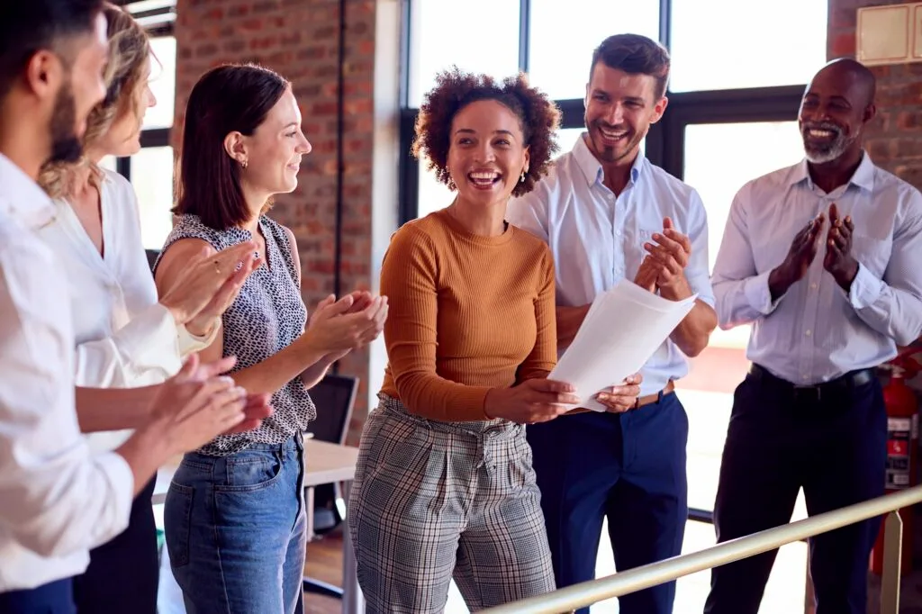 Colleagues Applauding Businesswoman Leading Team Meeting In Busy Multi-Cultural Office